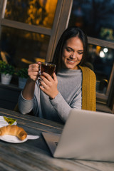 Shot of beautiful woman enjoying a cup of tea with her laptop open in front of her