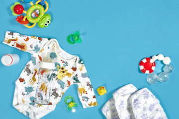 Babies goods: cloth diaper, baby powder, nibbler, cream, teether, soother, baby toy on blue background. Copy space. Top view.
