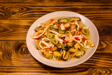 Ceramic plate with different sea food and olives on wooden table