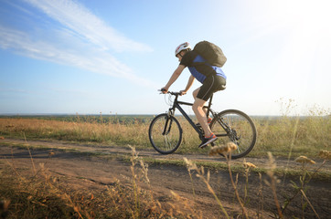 Male cyclist with backpack driving by rural dirt road outdoors