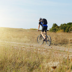 Male cyclist with backpack driving by rural dirt road outdoors