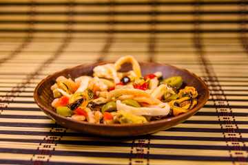 Ceramic plate with different sea food and olives on a bamboo mat