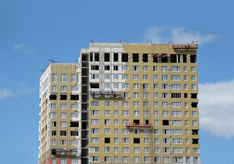 Process of mounting insulation on apartment building facade in new modern urban house over blue sky with clouds front view close up