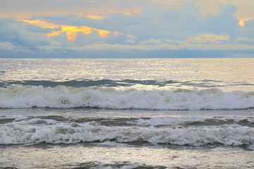 The waves beat at the beach with orange sky and white clouds in the morning. Soft focus. Nature background concept.