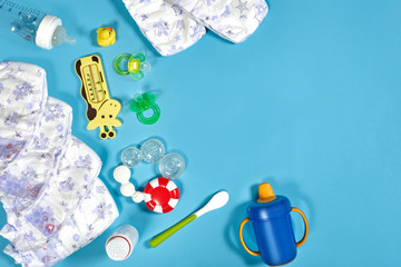 Babies goods: cloth diaper, baby powder, nibbler, cream, teether, soother, baby toy on blue...