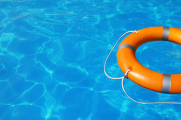 Lifebuoy floating in swimming pool on sunny day. Space for text