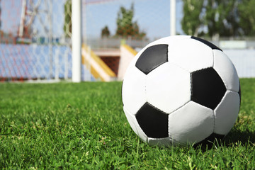 Soccer ball on green football field grass against net. Space for text