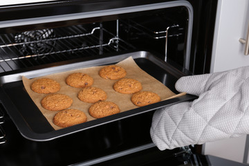 Woman taking baking tray with delicious cookies out of electric oven, closeup