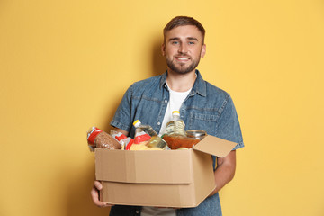 Young man holding box with donations on color background