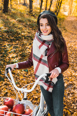 Fototapeta na wymiar fashionable young woman in leather jacket and beret carrying bicycle in forest