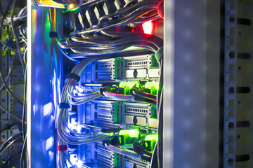 Modern server equipment works in a data center rack. Network interfaces and wires are in a dark...