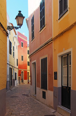 Fototapeta na wymiar A beautiful narrow quiet street of brightly painted old houses in summer sunlight in ciutedella menorca