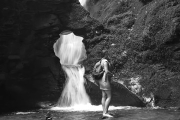 A black and white photograph of a young woman exploring a waterfall