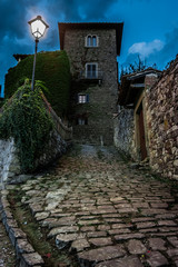 Prospettiva della torre del borgo di Montefioralle all'ingresso del paese con rampa in salita e piante rampicanti sul muro della casa, foto scattata di sera con lampione illuminato