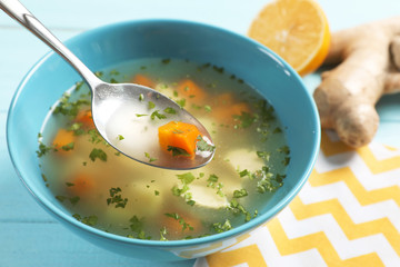 Spoon with fresh homemade soup to cure flu over bowl on wooden table