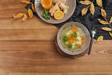 Flat lay composition with bowl of fresh homemade soup to cure flu and space for text on wooden...