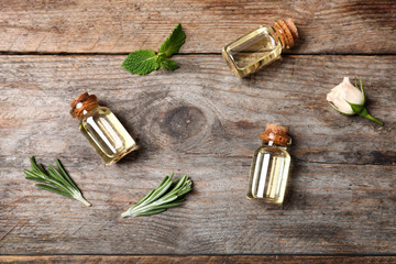 Fototapeta na wymiar Different essential oils in glass bottles and ingredients on wooden background, flat lay