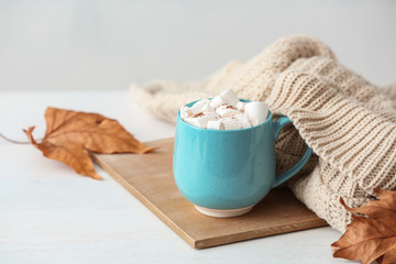 Obraz na płótnie Canvas Cup of hot cozy drink with marshmallows and autumn sweater on table. Space for text
