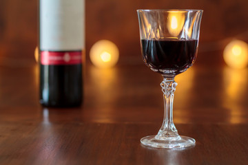 Glass of red wine on wooden table with the bottle in the background