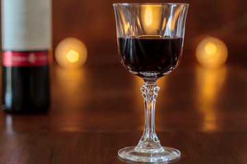 Crystal glass with red wine on wooden table with light bokeh in background