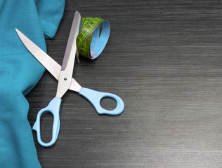 Blue color cloth, tailoring scissors and sartorial meter on wooden table for background. Fabric texture. Copy space.Top view.