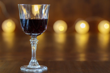 Glass with red wine on wooden table with lights in the background