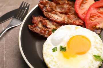 Pan with fried sunny side up egg, bacon and tomato on table, closeup