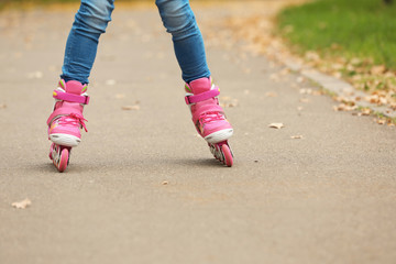 Fototapeta na wymiar Cute girl roller skating in autumn park, focus on legs. Space for text