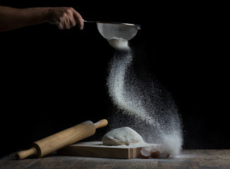 Flour is sprinkled over a ball of dough on a wooden board with roller