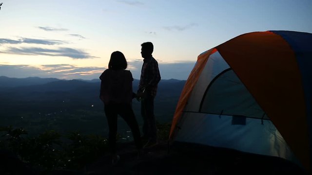 Camping trip of couple standing on the hill watching sunset twilight.