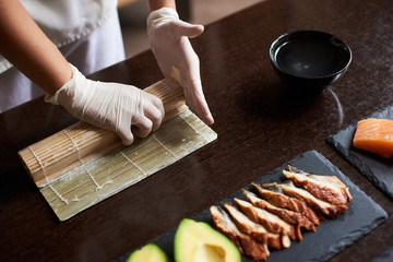 Closeup view of process of preparing rolling sushi. Master's hands making a sushi roll with bamboo...