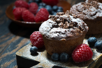 chocolate muffins and fresh berries on wooden board, closeup