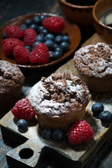chocolate muffins and fresh berries on wooden board, vertical top view