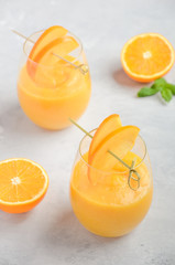 Fresh healthy smoothie with persimmon, orange and ginger on gray concrete background.