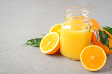 Fototapeta na wymiar Fresh orange juice in a jar on gray concrete background, selective focus, copy space.