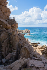 Fototapeta na wymiar Costa rocciosa con mare in vista, poche nuvole, bella giornata di sole e sentiero nella roccia