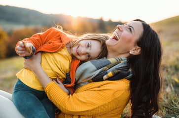 A portrait of young mother with a small daughter in autumn nature at sunset.
