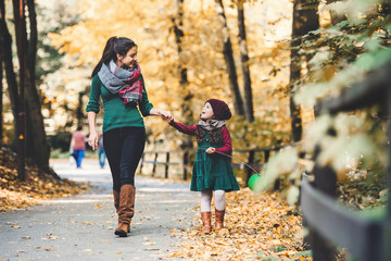 A young mother with a toddler daughter walking in forest in autumn nature.