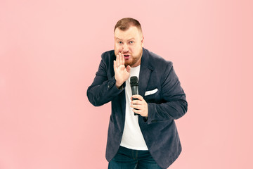 Young man with microphone on pink background, leading with microphone at studio concept. Human...