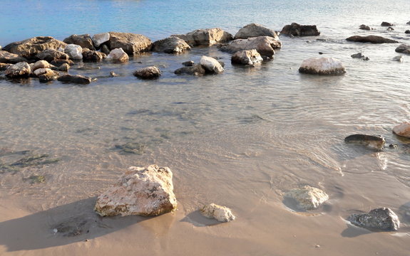 Sea shore with sand and rocks and rocks in the water at sunset, close-up with space for text