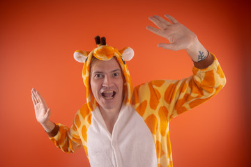 pajamas in the form of a giraffe. emotional portrait of a guy on an orange background. crazy and...