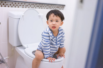 Little boy poo and pee in white toilet.