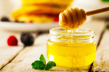 Honey with wooden honey dipper on wooden table