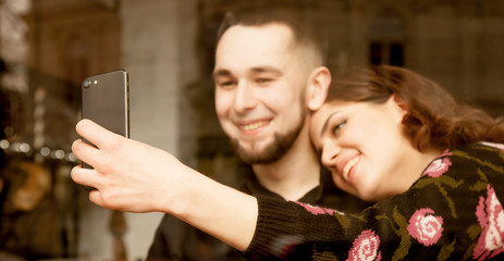 Embrace happiness, tenderness and love. Young couple hug each other and  taking selfie at cafe, view through a window.