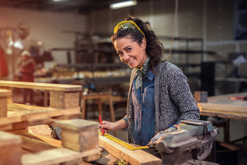 Middle aged professional female carpenter looking at the camera while taking measures of raw wood...