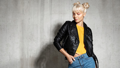 Stylish woman wearing leather jacket. Young blond-haired female posing in studio on cement...
