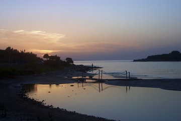 Ormos odyssea beach - kerenza near Parga at sunset, with a creek and a small bridge, silhouette of a fisherman fishing in the background