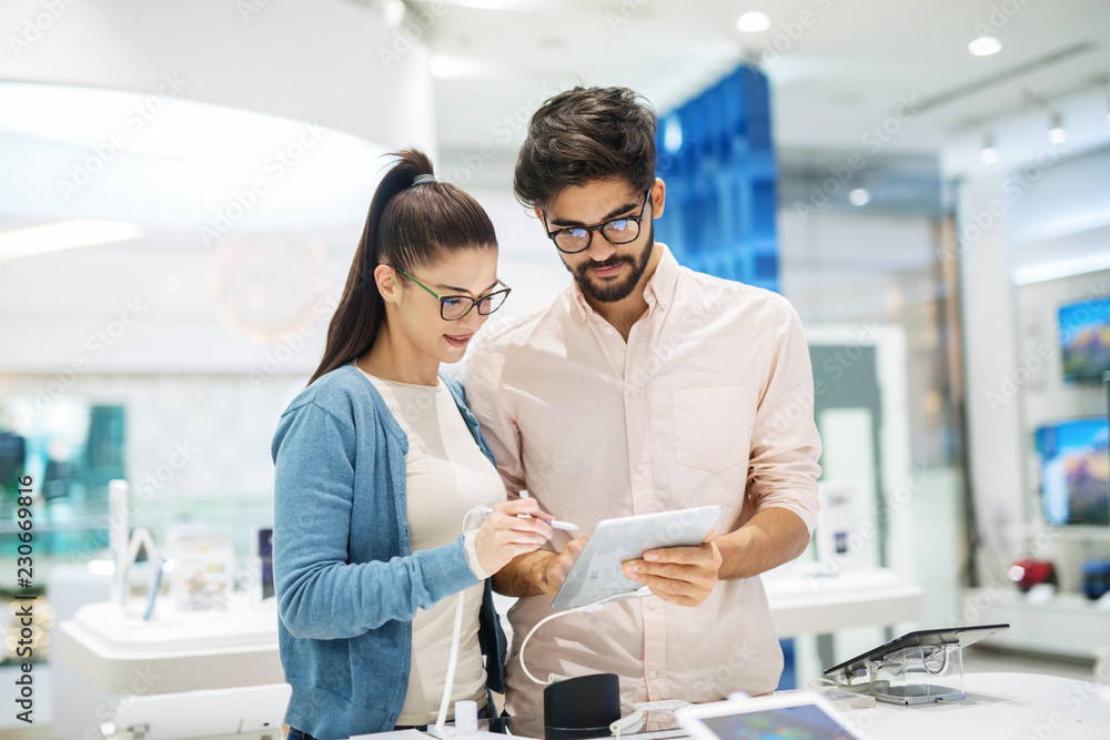 Canvas Prints Cheerful cute couple choosing new tablet in electronic store. Looking at tablet and smiling.