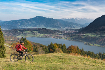 nice senior woman, riding her E-mountainbike in the indian summer on the mountains above the Alpsee near Immenstadt, Allgaeu, Bavaria, Germany