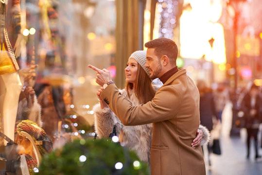 A beautiful young couple walking on the street and checking the storefront with christmas decoration.